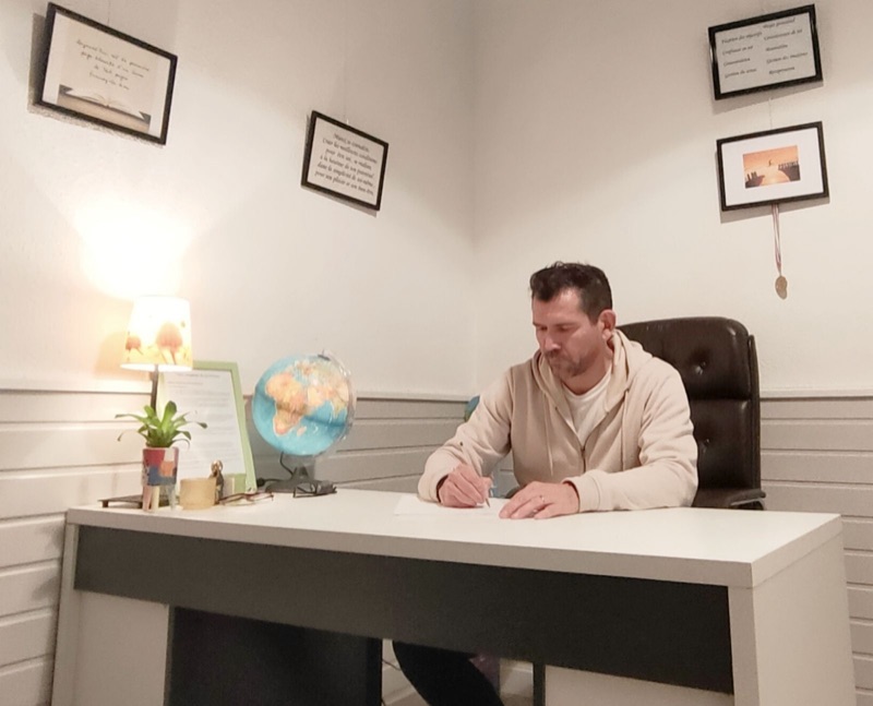 Diego Lacombe écrit à son bureau, entouré de cadres accrochés au mur